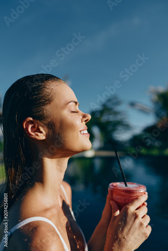 Cuadro en lienzo Sunny poolside moment features a smiling woman enjoying a pink smoothie, sipping through a straw, with water, palm trees and bright daylight in the background