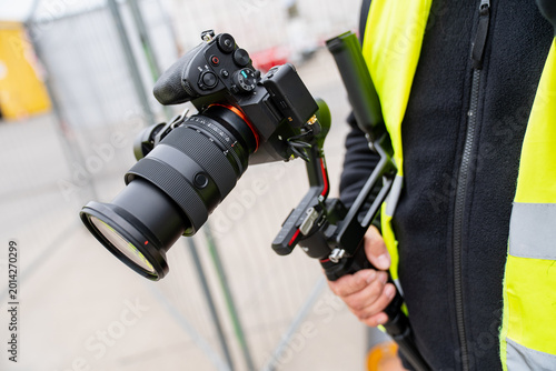 Videographer using a digital camera with a large lens and electronic steadycam system for high quality content production at a construction facility work zone
