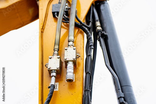 Hydraulic hoses and metal fittings on yellow construction machinery boom, showing equipment maintenance, fluid power, and heavy industry detail