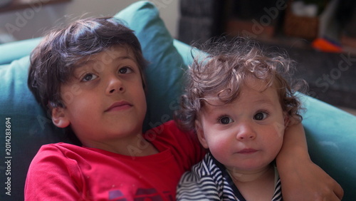 Φωτογραφία Older sibling holding toddler close on couch while giving gentle affectionate ki