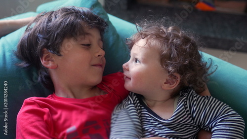 Photography Older sibling holding toddler close on couch while giving gentle affectionate ki