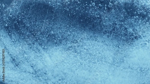 Extreme macro close-up of cracked blue melting ice texture in time lapse. Abstract frozen water surface with translucent crystal patterns, condensation and thawing details in studio lighting.