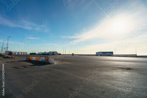 A wide angle view of a highway rest stop in Egypt with parked trucks and trailers under a clear blue sky during a sunny day.