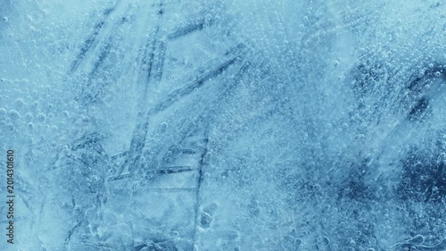 Extreme macro close-up of cracked blue melting ice texture in time lapse. Abstract frozen water surface with translucent crystal patterns, condensation and thawing details in studio lighting.