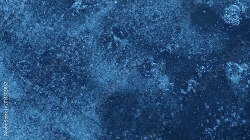 Extreme macro close-up of cracked blue melting ice texture in time lapse. Abstract frozen water surface with translucent crystal patterns, condensation and thawing details in studio lighting.