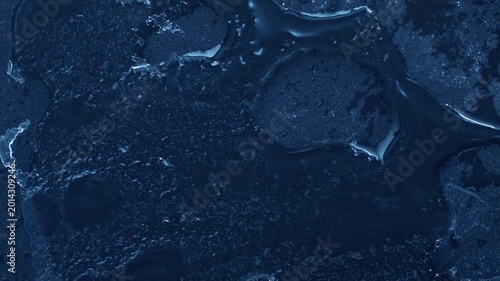 Extreme macro close-up of cracked blue melting ice texture in time lapse. Abstract frozen water surface with translucent crystal patterns, condensation and thawing details in studio lighting.