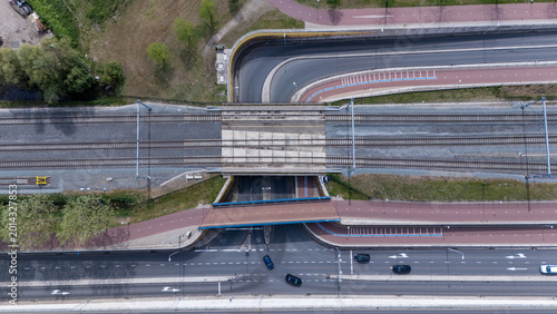 Top down aerial view of Dutch transport infrastructure with railway tracks, bicycle paths and car roads crossing each other. Urban mobility network showing different forms of transportation in holland