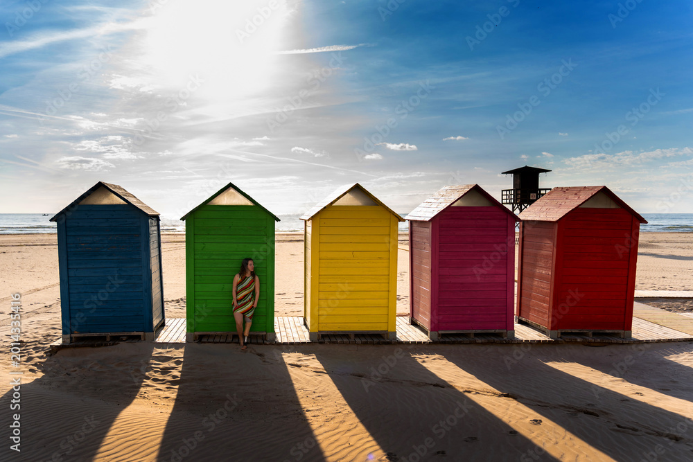 Fototapeta premium Woman with a prosthetic leg posing by vibrant beach huts, feeling inclusive and free