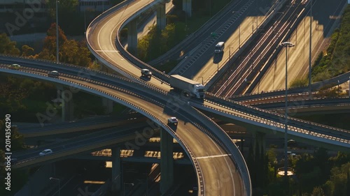 High-angle view of a bustling urban highway interchange with intricate ramps and overpasses, showing vehicles and trucks driving in multiple directions during a beautiful sunny day