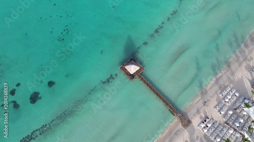 Aerial shot of a wooden pier with a brown roof extending into the vibrant turquoise waters contrasting with the white sandy beach,summer concept,La Romana, dominican republic.