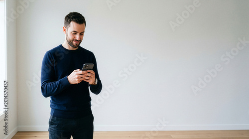 A modern man, absorbed in the glow of his mobile device, stands in thoughtful contemplation, exuding a sense of calm and connectivity.