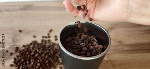 Person pours coffee beans into a silver container on a wooden surface in a kitchen setting