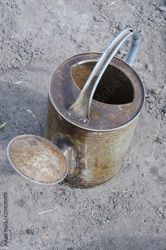 Old watering can on the ground in the garden, closeup of photo.