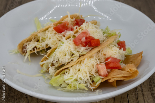 Foto Hearty plate of hard shell tacos smothered in lettuce, cheese, and pico to satis