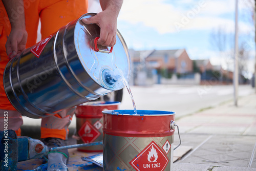 Quadro su tela Worker pours liquid solvent into blue road marking paint in a bucket preparing materials for application on asphalt while managing flammable substances safely