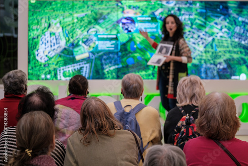 Tableau sur toile Group of seniors listening to urban planning presentation, speaker gestures toward large digital map, community engagement, public meeting