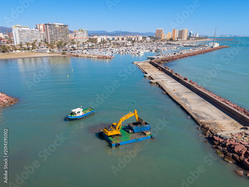 Fotografija Yellow excavator on floating barge performs harbor dredging near a breakwater je