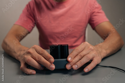Cropped shot of videographer inserting red lithium-ion camera battery into gray digital charger, preparing photographic equipment for event, ensuring power autonomy.