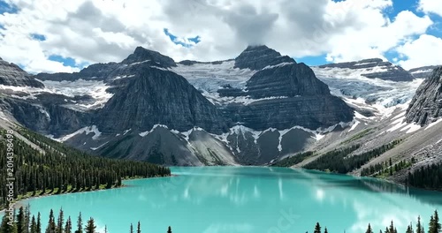 Majestic turquoise glacial lake surrounded by snow-capped mountains and dense evergreen forest under cloudy sky