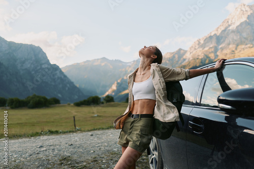Foto A confident woman leans against an open car door in a mountainous valley, basking in sunlit air and pine scent