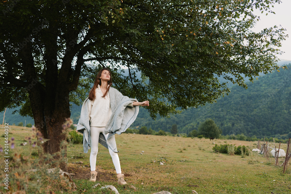 Fototapeta premium Casual lifestyle portrait of a woman standing in a grassy field with trees in the background, relaxed pose, soft natural light, open landscape, serene outdoor mood