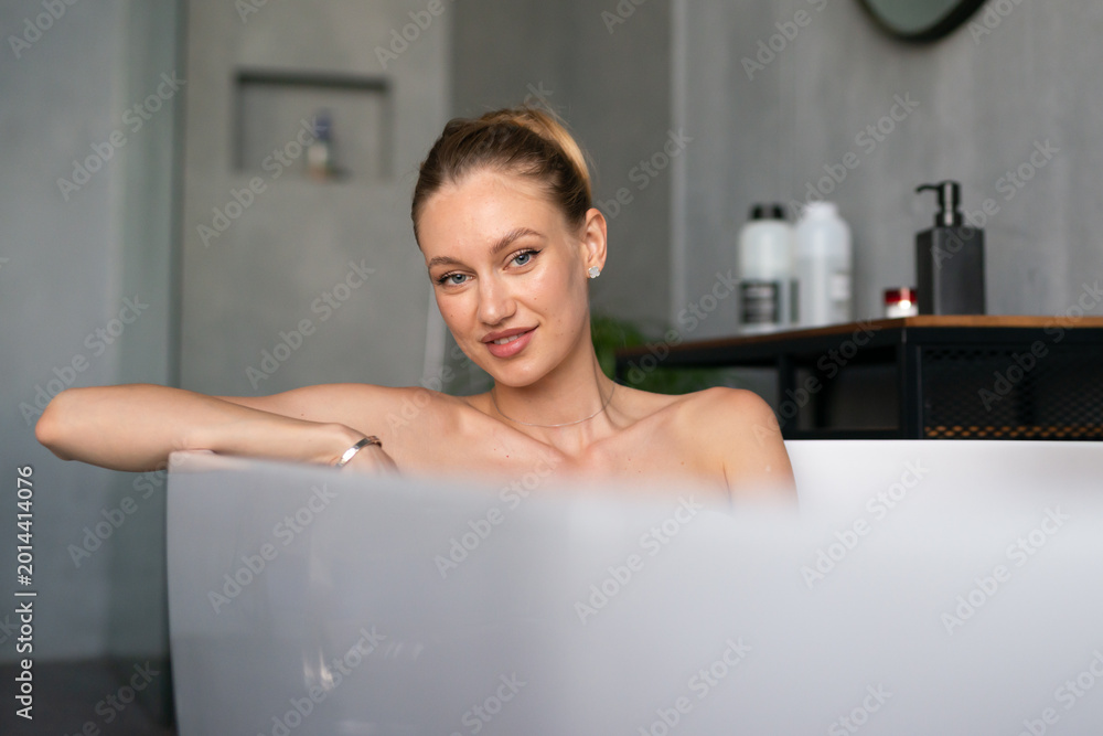 Obraz premium Woman in a modern bathroom soaking in a bathtub, finding calm and relaxation during personal self care time, promoting well being and a peaceful lifestyle