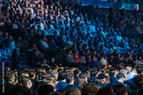 Schilderij op canvas Large indoor audience sitting in packed arena, blue lighting, attentive spectators at live performance, communal atmosphere, entertainment event