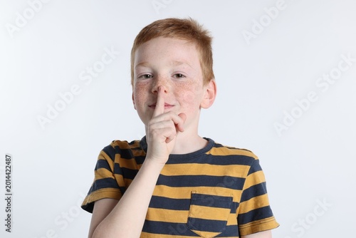Quadro su tela Little boy showing hush gesture on white background
