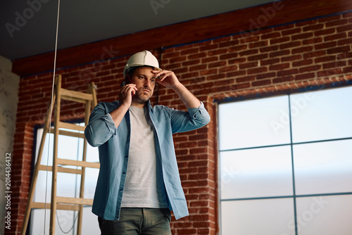 Obraz na płótnie Worried building contractor receiving bad news over cell phone during home renovation project