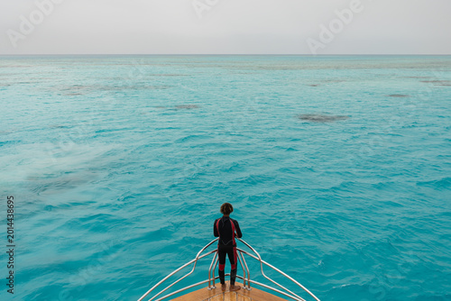 Foto Scuba diver in a wetsuit standing on the yacht bow and looking at the turquoise