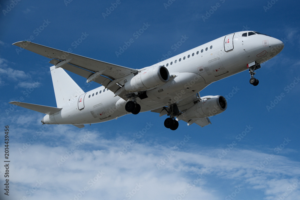 Fototapeta premium White Airplane Approaching for Landing Against Blue Sky with Clouds