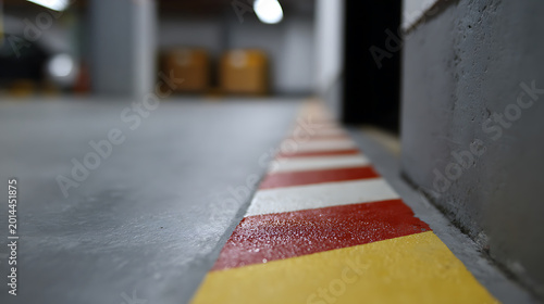 Low angle view of a yellow line with red and white hazard stripes on a concrete floor in an underground car park or industrial space