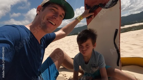 Father and son resting after sand boarding on tropical sand dunes - authentic family video