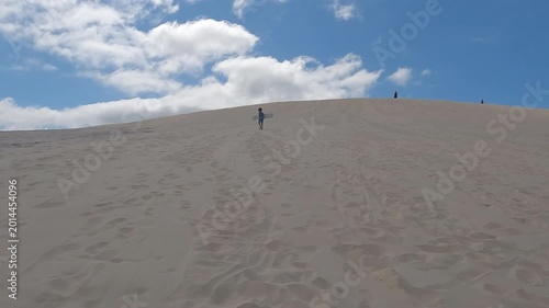 Young boy walking up sand dunes with sand board on tropical summer vacation - fun activities