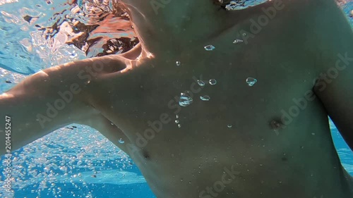 Young boy swimming in outdoor pool in tropics happily waves to camera underwater