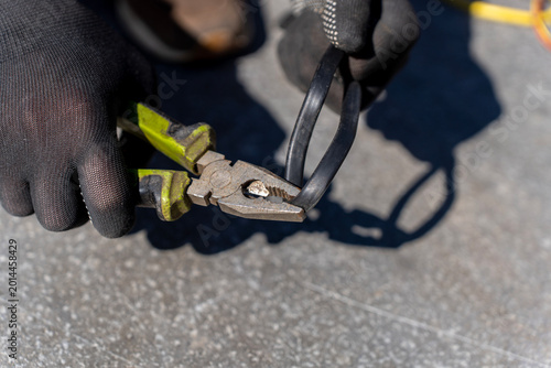 Cuadro en lienzo Worker grips black electrical cable with pliers while wearing protective gloves during outdoor cable repair or installation
