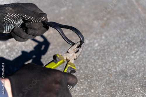 Schilderij op canvas Worker grips black electrical cable with pliers while wearing protective gloves during outdoor cable repair or installation