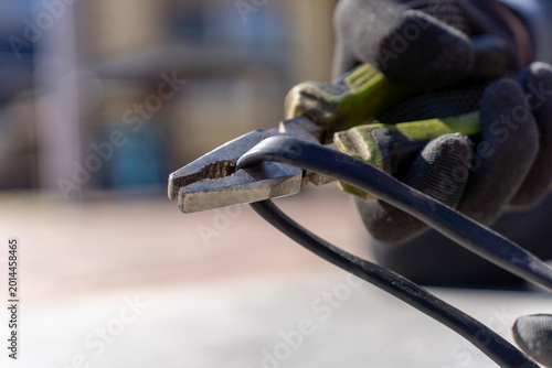 Foto Worker grips black electrical cable with pliers while wearing protective gloves during outdoor cable repair or installation
