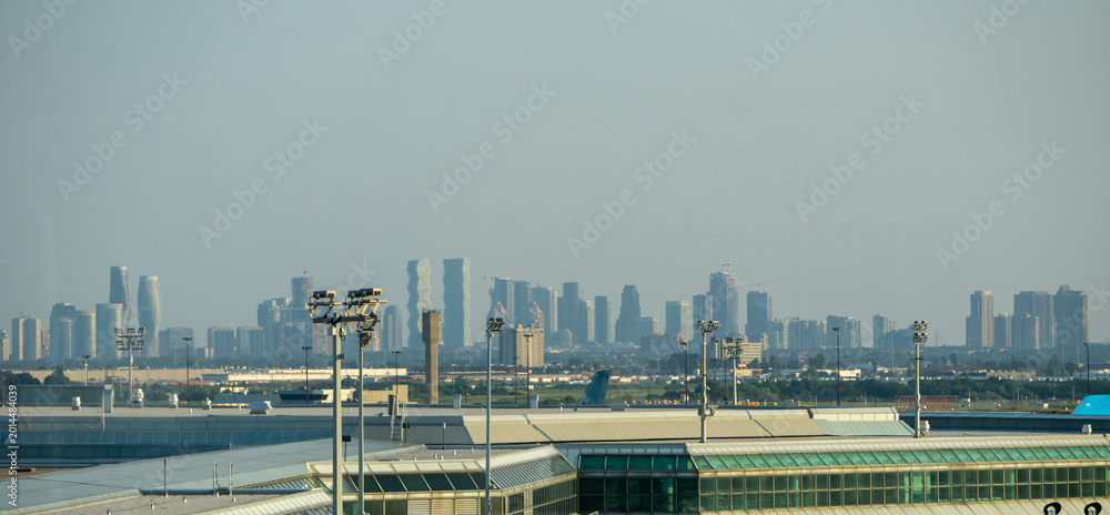 Fototapeta premium Distant Toronto Skyline Rising Beyond Airport Infrastructure Under Hazy Summer Atmosphere