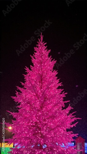 Pink christmas tree with lights glowing in the city at night. Holiday celebration decoration.