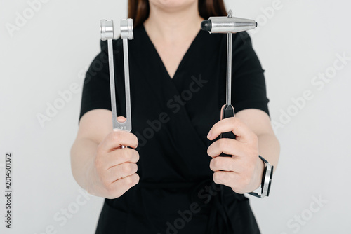 young woman doctor, medician in black costume, neurologist holds tuning fork and neurological reflex hammer for testing human reflexes in hands, medical services, tools and equipment for treatment