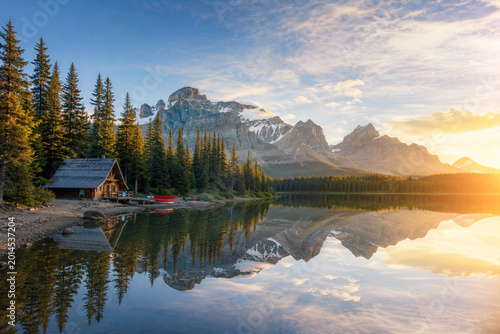 Rustic log cabin on alpine lake with mountain reflection at sunrise