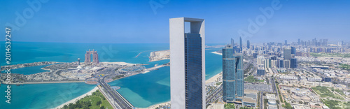 Wide panorama of the Abu Dhabi city skyline featuring waterfront skyscrapers along the Corniche, and the Arabian Gulf in the United Arab Emirates.