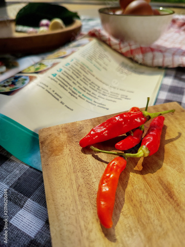 Fotografie Spicy Red Chilies on a Wooden Board Next to an Open Recipe Book, Perfect for Cul