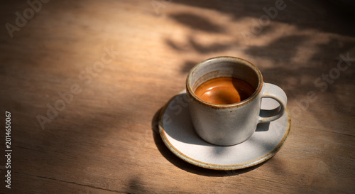 espresso coffee shot serving in small mug on wooden table in sun light and shade of wood branches and leaves