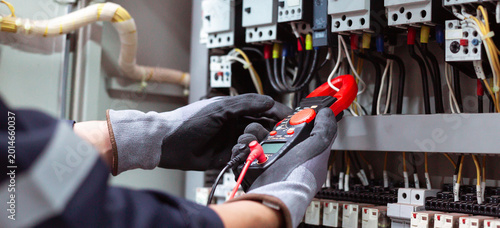 Photos Close-up of technician measuring amperage with clamp multimeter in industrial electric cabinet