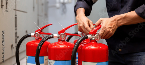 Professional technician checking and inspecting pressure gauge of red fire extinguishers for annual safety maintenance and compliance in industrial building.