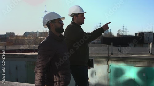 Two Professionals Walking Rooftop Together Discussing Timeline Tasks And Referencing Tablet For Coordination. Media