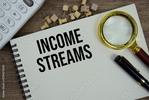 Income Streams text written on notepad with calculator and magnifying glass flat lay on wooden background