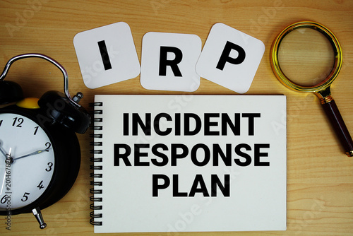 IRP  Incident Response Plan text written on notepad with magnifying glass and alarm clock on wooden background